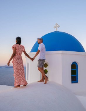 Men and women visit the whitewashed Greek village of Oia Santorini, a couple watching the sunrise in Santorini with blue domes and white churches