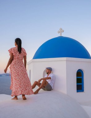 Men and women visit the whitewashed Greek village of Oia Santorini, a couple watching the sunrise in Santorini with blue domes and white churches