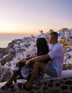 Couple visit Santorini Greece, men and women visit the whitewashed Greek village of Oia during summer vacation at sunrise over the blue domes and white churches