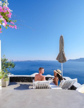 Men and women visit the whitewashed Greek village of Oia during a vacation in Santorini with blue domes and white churches in the village. 