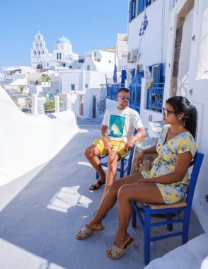 Men and women visit the whitewashed Greek village of Oia during a vacation in Santorini with blue domes and white churches in the village. 