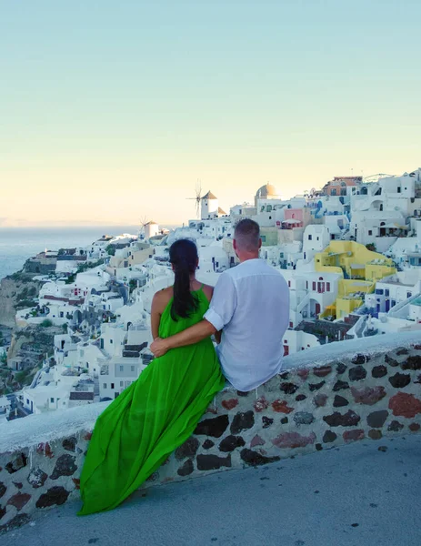 Couple watching the sunset on vacation in Santorini Greece, men and women watching the village with white churches and blue domes in Greece.