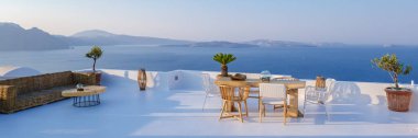outside terrace of a restaurant by the ocean of Santorini Greece, chairs, and tables with flowers by the ocean. 