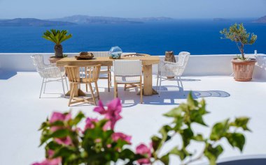 outside terrace of a restaurant by the ocean of Santorini Greece, chairs, and tables with flowers by the ocean. 