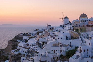 Sunset with white churches an blue domes by the ocean of Oia Santorini Greece.