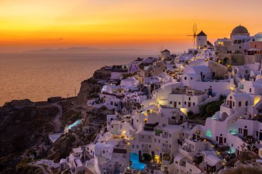 Sunset with white churches an blue domes by the ocean of Oia Santorini Greece.