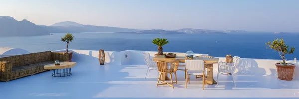 outside terrace of a restaurant by the ocean of Santorini Greece, chairs, and tables with flowers by the ocean.