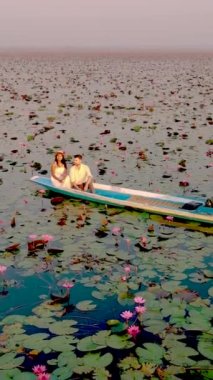 Sunrise at The sea of red lotus, Lake Nong Harn, Udon Thani, Thailand. Couple of men and women in a wooden boat during sunrise at the red lotus lake in Thailand