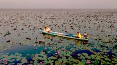 Sunrise at The sea of red lotus, Lake Nong Harn, Udon Thani, Thailand. Couple of men and women in a wooden boat during sunrise at the red lotus lake in Thailand