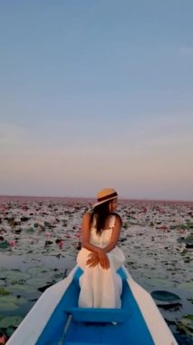 Gündoğumu Kızıl Nilüfer Denizi, Nong Harn Gölü, Udon Thani, Tayland. Tayland 'daki Red Lotus Gölü' nde güneş doğarken tahta bir teknede Asyalı bir kadın. 