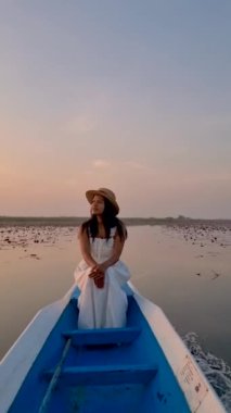 Gündoğumu Kızıl Nilüfer Denizi, Nong Harn Gölü, Udon Thani, Tayland. Asyalı bir kadın, güneş doğarken tahta bir teknede Tayland 'daki kırmızı lotus gölünde. 