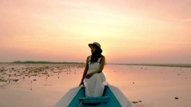 Sunrise at The sea of red lotus, Lake Nong Harn, Udon Thani, Thailand. A Asian women in a wooden boat during sunrise at the red lotus lake in Thailand 