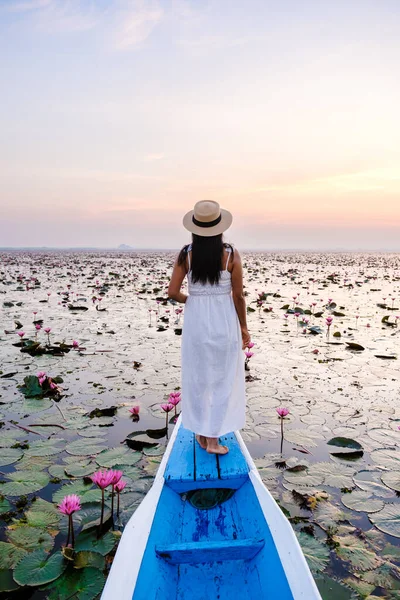 Asian women in a boat at the Beautiful Red Lotus Sea Kumphawapi is full of pink flowers in Udon Thani in Northern Thailand Isaan. Flora of Southeast Asia.