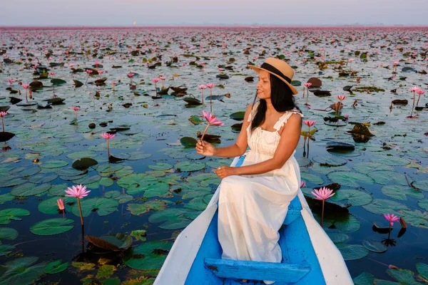 Asian women in a boat at the Beautiful Red Lotus Sea Kumphawapi is full of pink flowers in Udon Thani in northern Thailand. Flora of Southeast Asia.