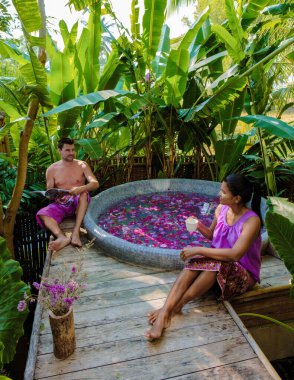 Tatil sırasında Tayland 'ın yağmur ormanlarında bir küvette dinlenen çift, erkekler ve kadınlar, dışarıda gül yapraklarıyla jakuzide dinleniyorlar.. 