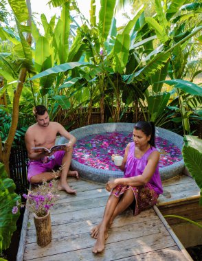 Tatil sırasında Tayland 'ın yağmur ormanlarında bir küvette dinlenen çift, erkekler ve kadınlar, dışarıda gül yapraklarıyla jakuzide dinleniyorlar.. 