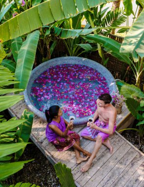 Tayland 'ın yağmur ormanlarındaki bir küvette bir çift, banyoda çiçeklerle birlikte, erkekler ve kadınlar jakuzide dinleniyor, dışarıda gül yaprakları ve kahve içiyorlar.