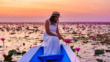 Asian women with a hat and dress in a boat at the Beautiful Red Lotus Sea Kumphawapi is full of pink flowers in Udon Thani in northern Thailand. Flora of Southeast Asia.