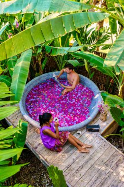 Tatil sırasında Tayland yağmur ormanlarındaki bir küvette banyo yapan bir çift, erkekler ve kadınlar dışarıda gül yapraklarıyla jakuzide dinleniyorlar. Gençler kitap okuyor.