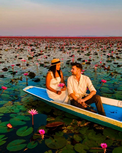 Sunrise at The sea of red lotus, Lake Nong Harn, Udon Thani, Thailand. Couple of men and women in a wooden boat during sunrise at the red lotus lake in Thailand