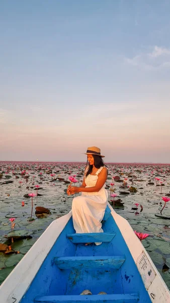 Asian women in a boat at the Beautiful Red Lotus Sea Kumphawapi is full of pink flowers in Udon Thani in Northern Thailand Isaan. Flora of Southeast Asia.