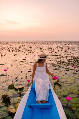 Taylandlı kadınlar kırmızı nilüfer denizinde, Nong Harn Gölü, Udon Thani, Tayland, Asyalı kadın elbise ve şapkalı kırmızı nilüfer ağacından bir teknede. 