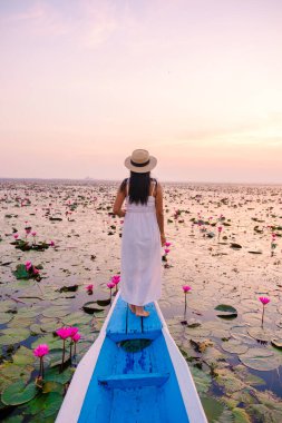 Taylandlı kadınlar kırmızı nilüfer denizinde, Nong Harn Gölü, Udon Thani, Tayland, Asyalı kadın elbise ve şapkalı kırmızı nilüfer ağacından bir teknede. 