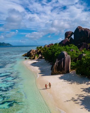 Anse Source dArgent plajı, La Digue Adası, Seyshelles, La Digue Seyşeller 'in insansız hava görüntüsü tropik adanın kuş bakışı görüntüsü, günbatımında sahilde yürüyen iki erkek ve kadın.