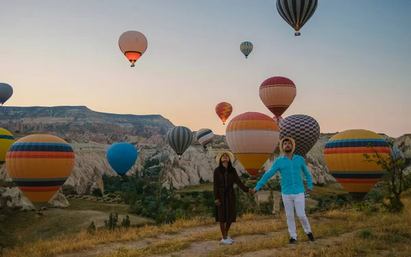 アジアの女性と白人男性中年カパドキヤカッパドキアへの旅行でトルコ 休暇中にカパドキヤカッパドキアトルコの熱気球を見ている日の出の間に幸せな若いカップル — ストック写真