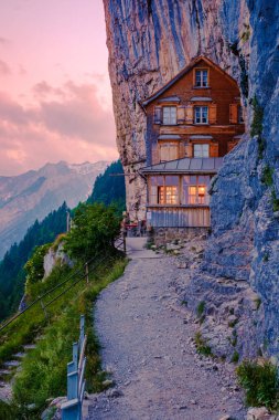 Gün batımında Den Appenzeller Alpen 'de Berggasthaus Aescher, İsviçre' de Ebenalp Dağı 'nda bir uçurumun altında restoran, yazın günbatımında Appenzell