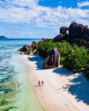 Anse Source dArgent plajı, La Digue Adası, Seyşeller, La Digue Seyşeller 'in insansız hava görüntüsü tropik adanın kuş bakışı görüntüsü, gün batımında sahilde yürüyen birkaç erkek ve kadın.