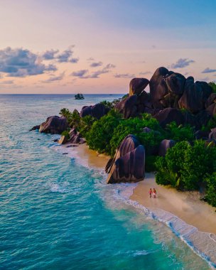 Anse Source dArgent plajı, La Digue Adası, Seyshelles, La Digue Seyşeller 'in insansız hava görüntüsü tropik adanın kuş bakışı görüntüsü, günbatımında sahilde yürüyen iki erkek ve kadın.