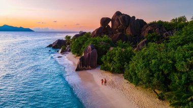 Anse Source dArgent plajı, La Digue Adası, Seyshelles, Seyshelles, İHA hava manzaralı La Digue Seyşeller çift ve kadın gün batımında lüks bir tatilde sahilde yürüyorlar.