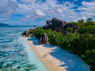 Anse Source dArgent plajı, La Digue Adası, Seyshelles, La Digue Seyşeller 'in insansız hava görüntüsü tropik adanın kuş bakışı görüntüsü, günbatımında sahilde yürüyen iki erkek ve kadın.