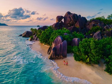Anse Source dArgent plajı, La Digue Adası, Seyshelles, La Digue Seyşeller 'in insansız hava görüntüsü tropik adanın kuş bakışı görüntüsü, günbatımında sahilde yürüyen iki erkek ve kadın.