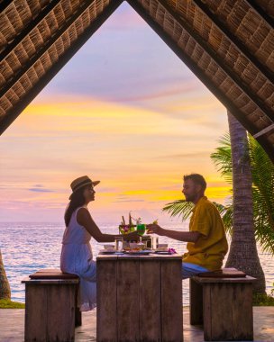 Romantic dinner on the beach with Thai food during sunset on the Island of Koh Mak Thailand. Couple of men and women having a romantic dinner on the beach clipart
