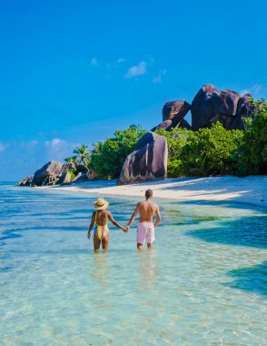 Anse Source dArgent plajı, La Digue Adası, Seyshelles, La Digue Seyşeller 'in insansız hava görüntüsü tropik adanın kuş bakışı görüntüsü, günbatımında sahilde yürüyen iki erkek ve kadın.
