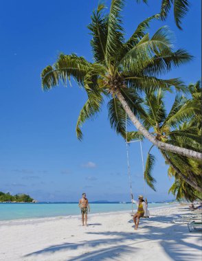 Praslin Seychelles tropical island with white beaches and palm trees, a couple of men and women in hammocks swing on the beach under a palm tree at Anse Volber Seychelles. clipart