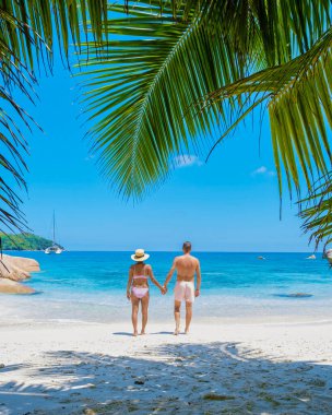 Anse Lazio Praslin Seyşeller. Tropikal bir plajda, Seyşeller 'de palmiye ağaçlarıyla plajda dinlenen genç bir çift.