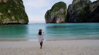 Maya Körfezi sahilinde yürüyen Taylandlı kadınlar Koh Phi Phi Tayland, sabahın erken saatlerinde sahilde turistsiz ve turkuaz renkli okyanussuz. 