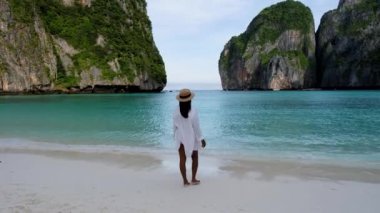 Maya körfezi sahilinde yürüyen Asyalı kadınlar Koh Phi Phi Tayland, sabahın erken saatlerinde sahilde turistsiz ve turkuaz renkli okyanussuz. 