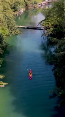 Tropikal ada Koh Chang Tayland 'da kano süren bir çift kadın ve erkek, güneş batarken Koh Chang ormanındaki tropikal bir nehirde kano manzaralı.