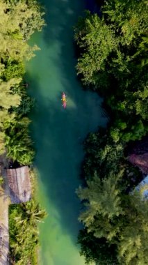 Tropikal ada Koh Chang Tayland 'da kano süren bir çift kadın ve erkek, güneş batarken Koh Chang ormanındaki tropikal bir nehirde kano manzaralı.