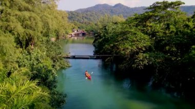 Tropikal ada Koh Chang Tayland 'da kano süren bir çift kadın ve erkek, güneş batarken Koh Chang ormanındaki tropikal bir nehirde kano manzaralı.