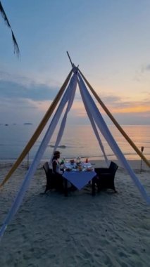 Tayland 'da gün batımında Koh Chang adasında romantik bir akşam yemeği. Kadınlar gün batımında sahilde yemek yiyorlar.