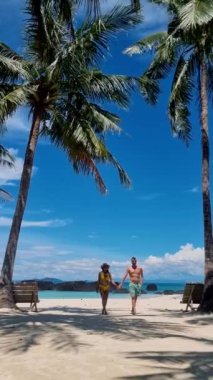 Tayland 'da palmiye ağaçlarıyla tropik beyaz kumlu sahilde yürüyen olgun bir çift. Erkekler ve kadınlar doğu Tayland 'daki Koh Kham Trat adasına tekne gezisine gittiler.