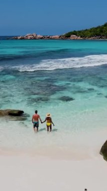 Anse Cocos plajı la Digue Seyşeller, tropikal ada La Digue Seyşeller 'de mayo giymiş iki adam okyanusta yürüyor.