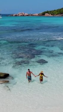 Anse Cocos plajı la Digue Seyşeller, tropikal ada La Digue Seyşeller 'de mayo giymiş iki adam okyanusta yürüyor.