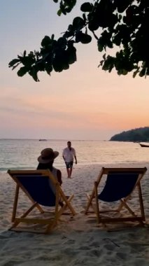 Çiftler tropikal plajda gün batımını izliyorlar, Asyalı kadınlar ve Koh Lipe Tayland sahilinde bir sandalyede beyaz erkekler..