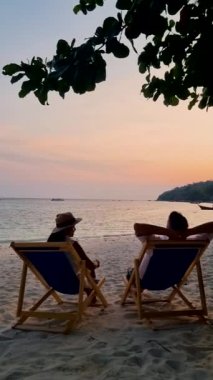 Çiftler tropikal plajda gün batımını izliyorlar, Asyalı kadınlar ve Koh Lipe Tayland sahilinde bir sandalyede beyaz erkekler..